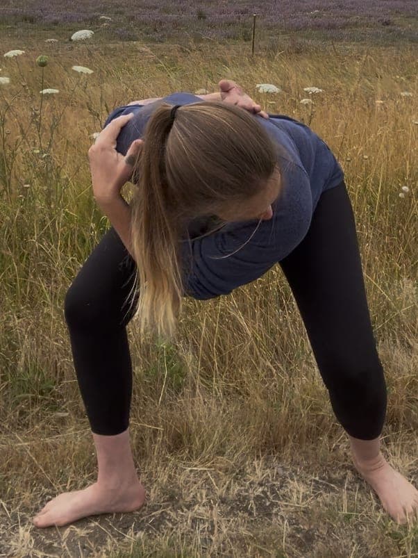 Maria demonstrating a standing forward-fold neck release in a lavender field