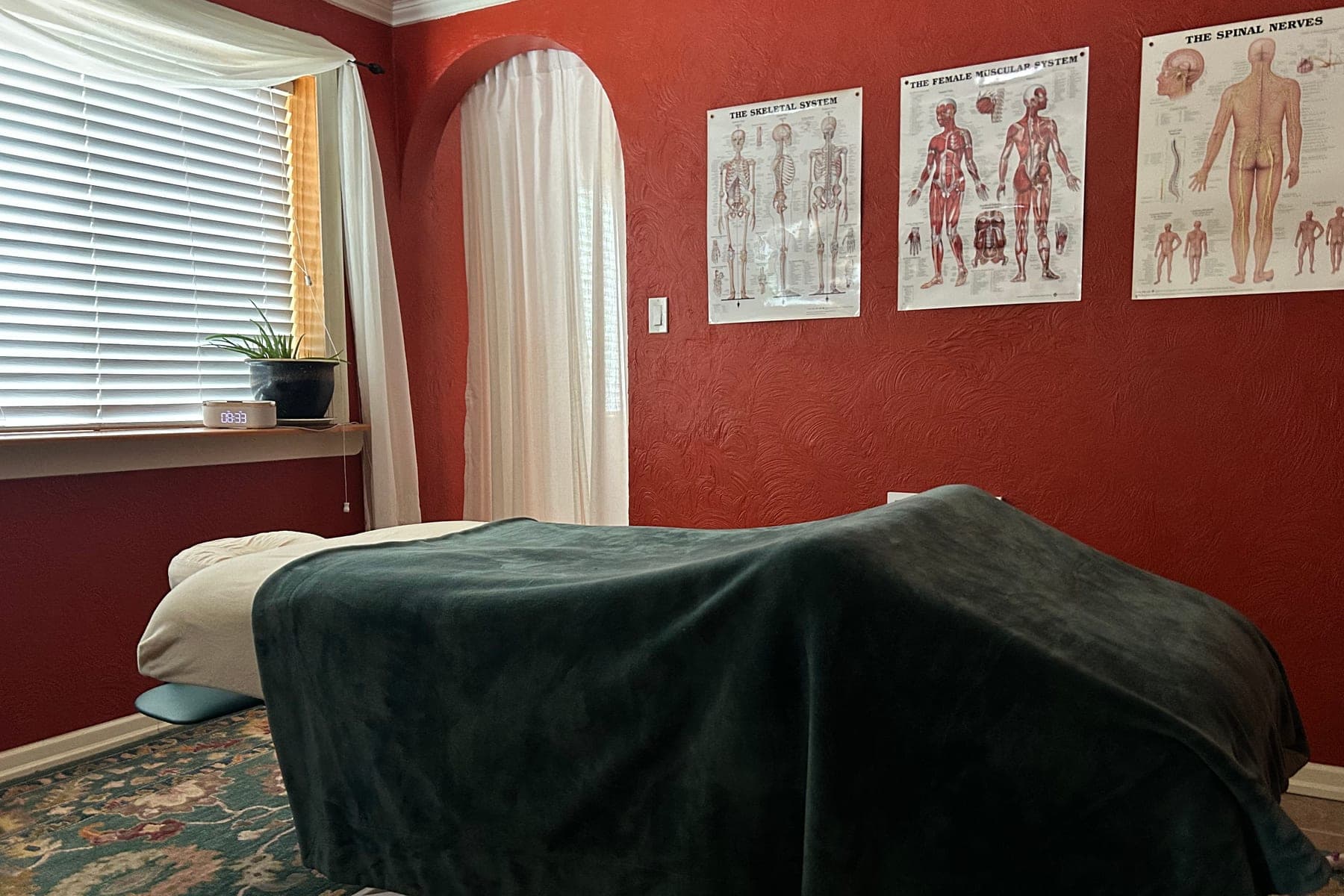 The treatment room at Body Harmony Massage, with a draped massage table, anatomy charts and a patterned rug
