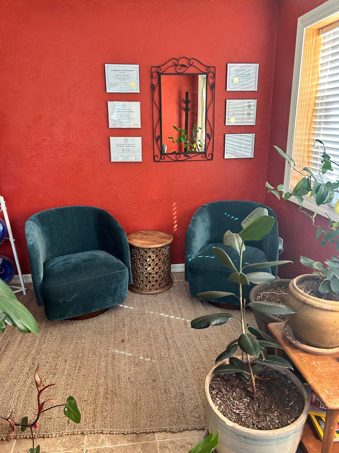 The waiting area at Body Harmony Massage, with two teal armchairs, houseplants and framed certificates