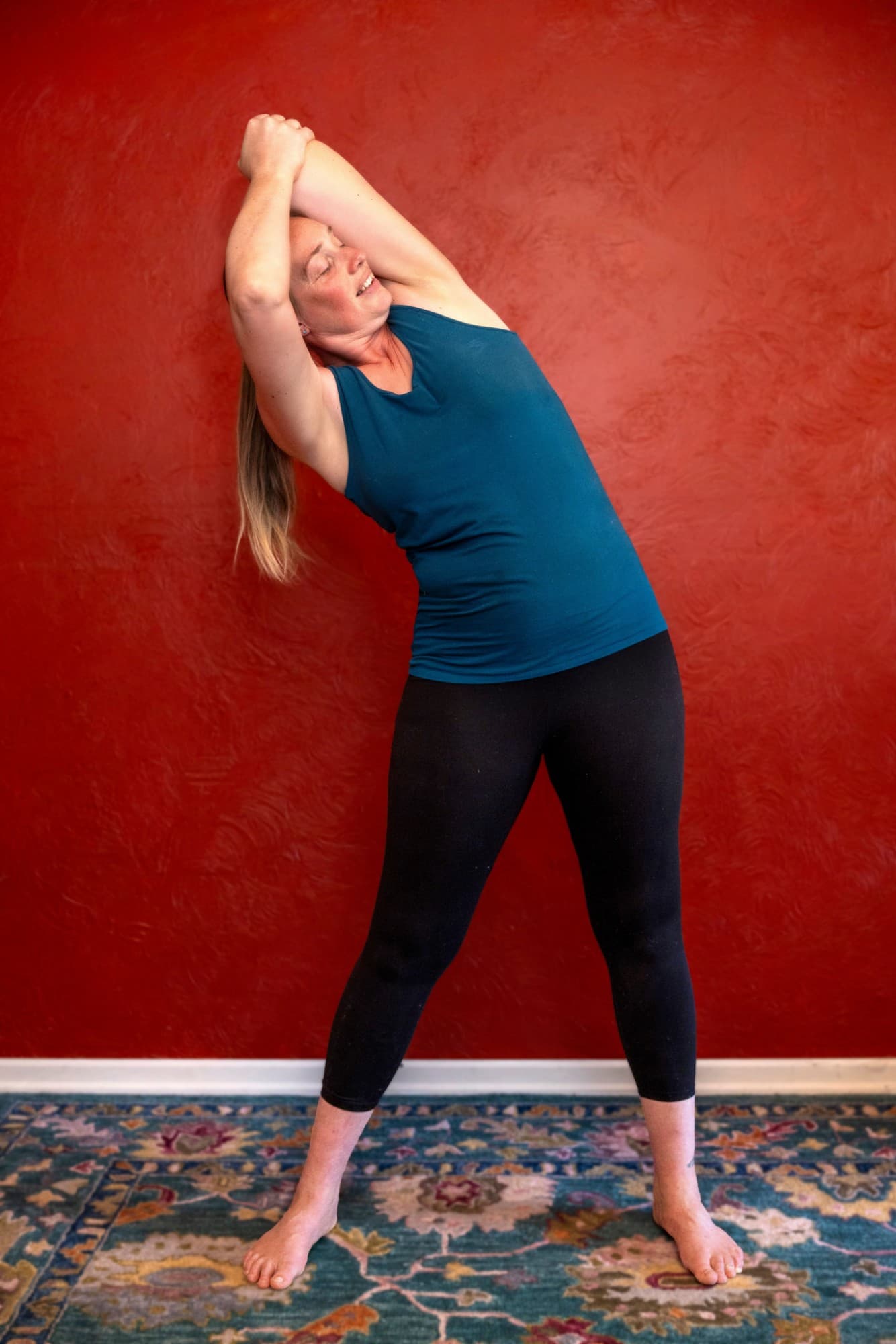 Maria demonstrating a standing side stretch, releasing through the arm and side body